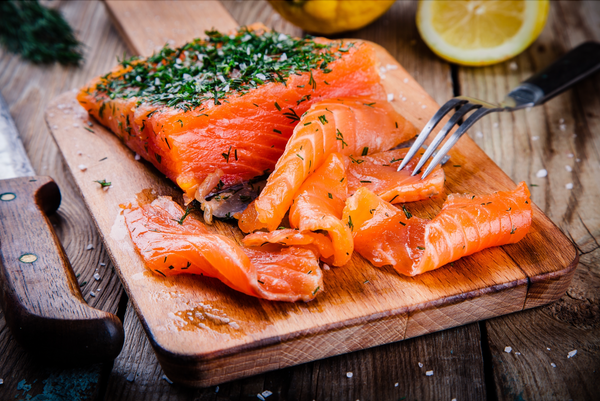 Smoked salmon fillet and slices garnished with herbs on a wooden cutting board with lemon slices