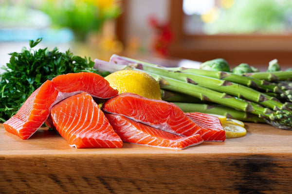 Four raw sockeye salmon fillets with lemon, asparagus, and parsley on a wooden cutting board