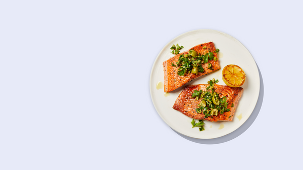 Two cooked salmon fillets garnished with herbs and a grilled lemon half on a white plate.