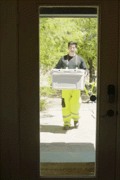 Person in high-visibility pants carrying a large box through a doorway outdoors