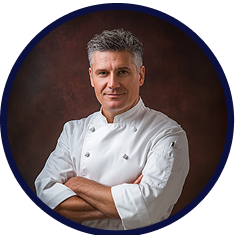 Chef in white uniform with arms crossed against a dark background