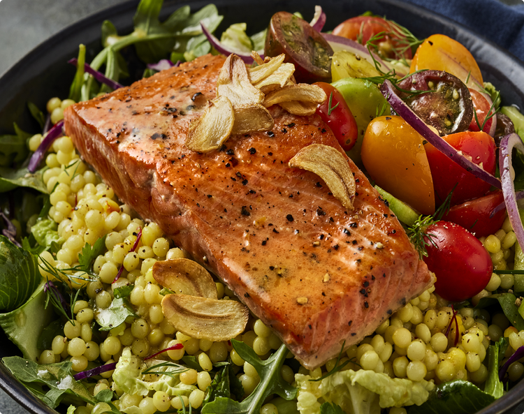 Salmon fillet on couscous-like salad with cherry tomatoes, mixed greens and crispy garlic chips
