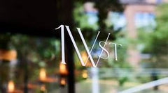 Stylized text '1W St' on a glass surface with blurred outdoor background