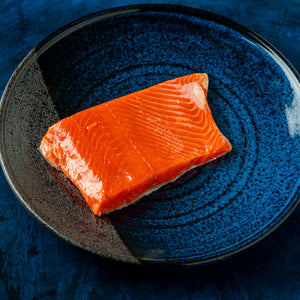 Raw salmon fillet on a blue ceramic plate against a dark background