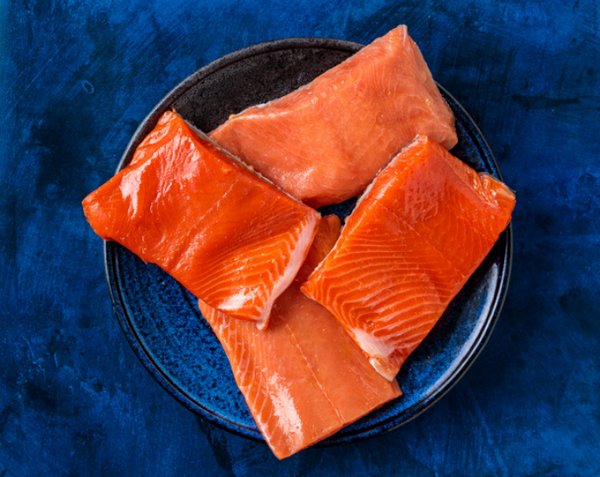 Four raw salmon fillets on a blue plate against a dark blue background.
