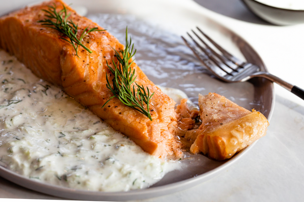 Cooked Alaskan sockeye salmon fillet topped with fresh dill, served with creamy dill sauce on a gray plate