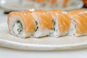 Salmon-topped sushi rolls with rice, cucumber and cream cheese on a round beige plate