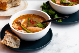 Bowl of salmon soup with asparagus, tomato and parsley, served with crusty bread on a dark saucer.