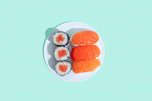 Three salmon nigiri and three salmon maki rolls on a white plate against a pale mint background.