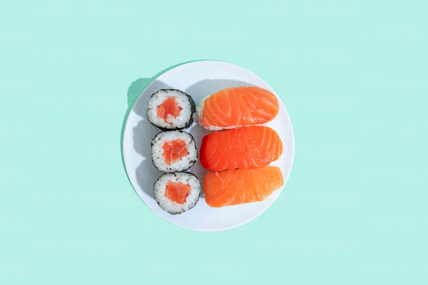 Three salmon nigiri and three salmon maki rolls on a white plate against a pale mint background.