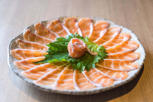 Thinly sliced nova lox arranged in a circular pattern on a plate with a green leaf garnish in the center