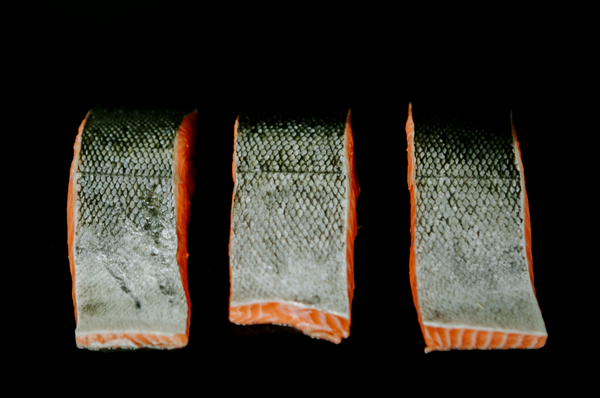 Three raw salmon fillets with skin on a black background.