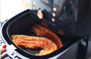 Breaded fish fillets in an air fryer basket as a person pulls the basket out