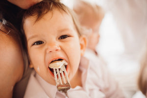Baby taking a bite from a fork while held by an adult