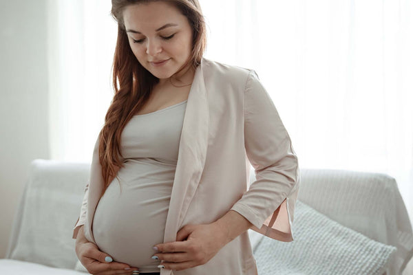 Pregnant woman gently cradling her belly in a softly lit living room