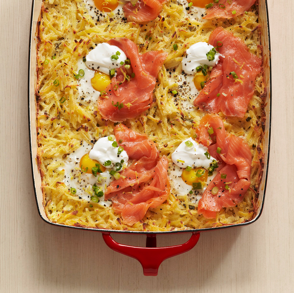 Baked hash brown casserole with eggs, smoked salmon, sour cream, and green onions in a red-handled pan