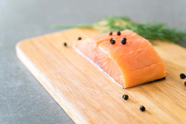 Raw salmon fillet on wooden cutting board with black peppercorns and dill sprig