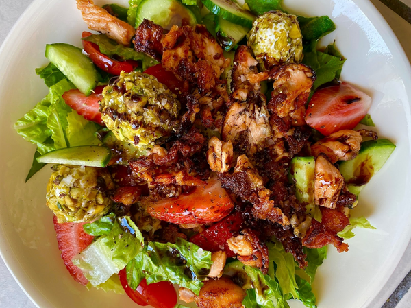 Salad with crispy salmon, strawberries, cucumber, lettuce, and pistachio-coated cheese balls