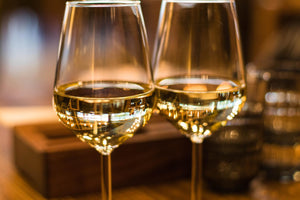 Two stemmed glasses of white wine with warm reflections on a wooden table, close-up.