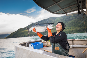 Person on a boat holding a large fish with mountains and water in the background