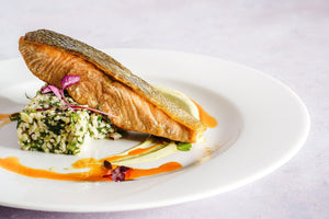 Cooked salmon fillet with crispy skin on a white plate with rice and sauce garnish