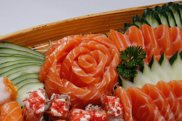 Salmon sashimi and sushi arranged with cucumber slices and parsley garnish on a wooden platter