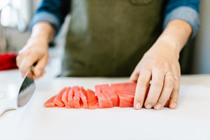 Person slicing raw red-fleshed fish into sashimi-style slices on a white cutting board