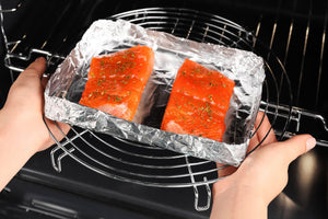 Two seasoned salmon fillets on foil being placed in an oven rack