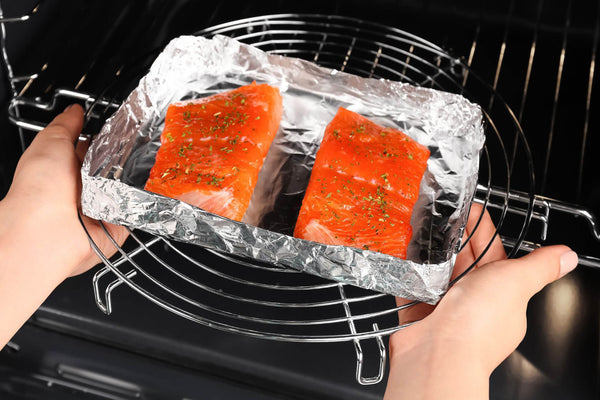 Two seasoned salmon fillets on foil being placed in an oven rack