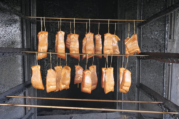 Pieces of salmon hanging on metal rods inside a smoker for smoking process