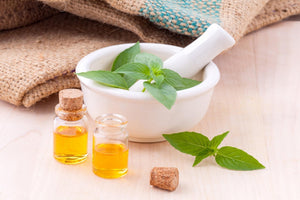 mortar and pestle with basil leaves and two small bottles of yellow oil on wooden surface
