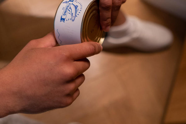 Hands holding a metal can labeled FISHING club with a fish logo