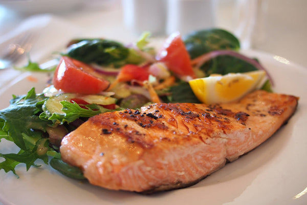 Grilled salmon fillet with mixed salad and lemon wedge on a white plate.