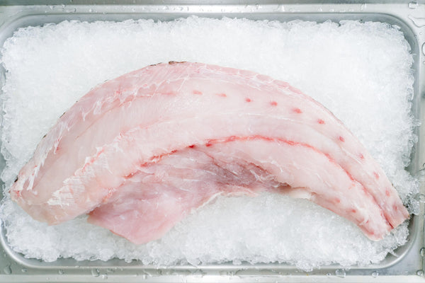 Raw pinkish fish fillet with faint red veins on crushed ice in a metal tray