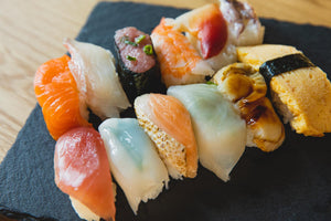 Assorted nigiri sushi (salmon, tuna, shrimp, scallop, tamago) arranged on a dark slate serving plate