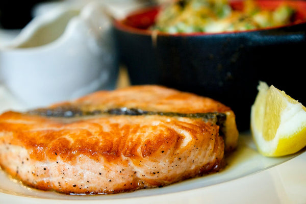 Close-up side view of seared salmon fillet showcasing crispy browned crust and lemon wedge on a white plate