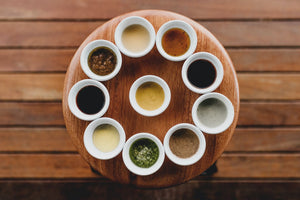 Ten small bowls of various sauces arranged in a circle on a round wooden table