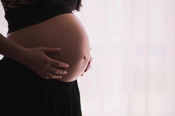 Pregnant woman's bare belly gently cradled by her hands