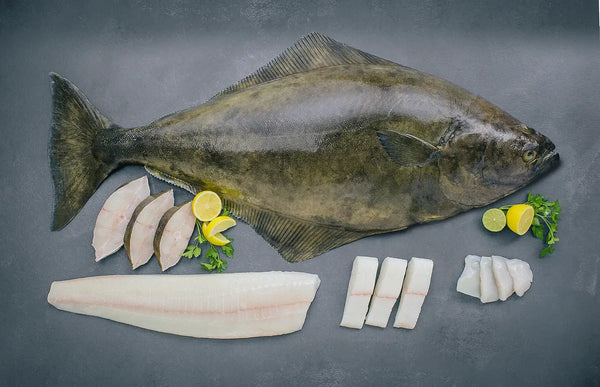 Whole halibut fish with sliced pieces, lemon, lime, and parsley on a gray surface