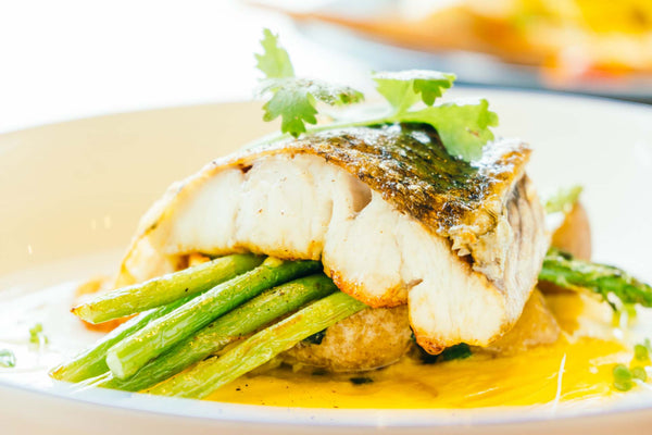 Cooked halibut fillet on green beans with sauce and a garnish on top