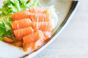 Orange salmon sashimi slices on a ceramic plate with lettuce and halved cherry tomato