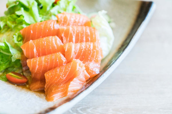 Orange salmon sashimi slices on a ceramic plate with lettuce and halved cherry tomato
