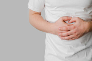 Person holding stomach with both hands, wearing a white shirt