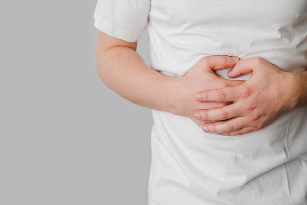 Person holding stomach with both hands, wearing a white shirt