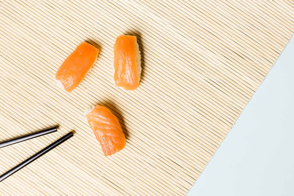 Three pieces of salmon nigiri sushi on a bamboo sushi rolling mat with black chopsticks