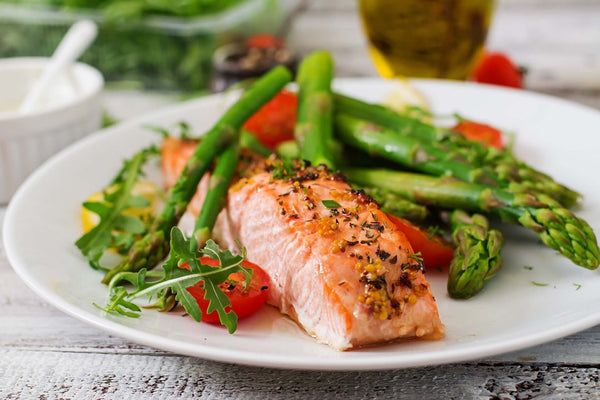 Baked salmon fillet served with asparagus, cherry tomatoes, and arugula on a white plate