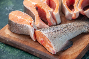 raw salmon steaks with skin on a wooden cutting board.