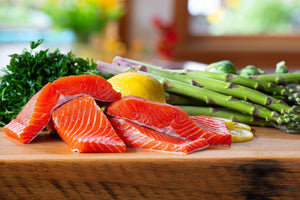 Four raw sockeye salmon fillets with lemon, asparagus, and parsley on a wooden cutting board