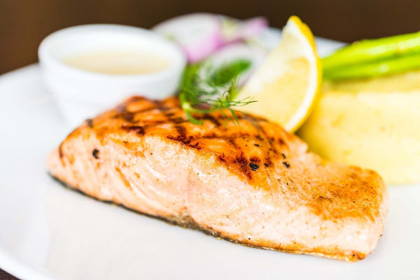 Pan-seared salmon on a white plate with lemon wedge, asparagus and a small sauce cup.