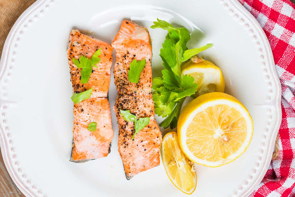 Two peppered salmon fillets garnished with parsley, served with lemon halves on a white plate